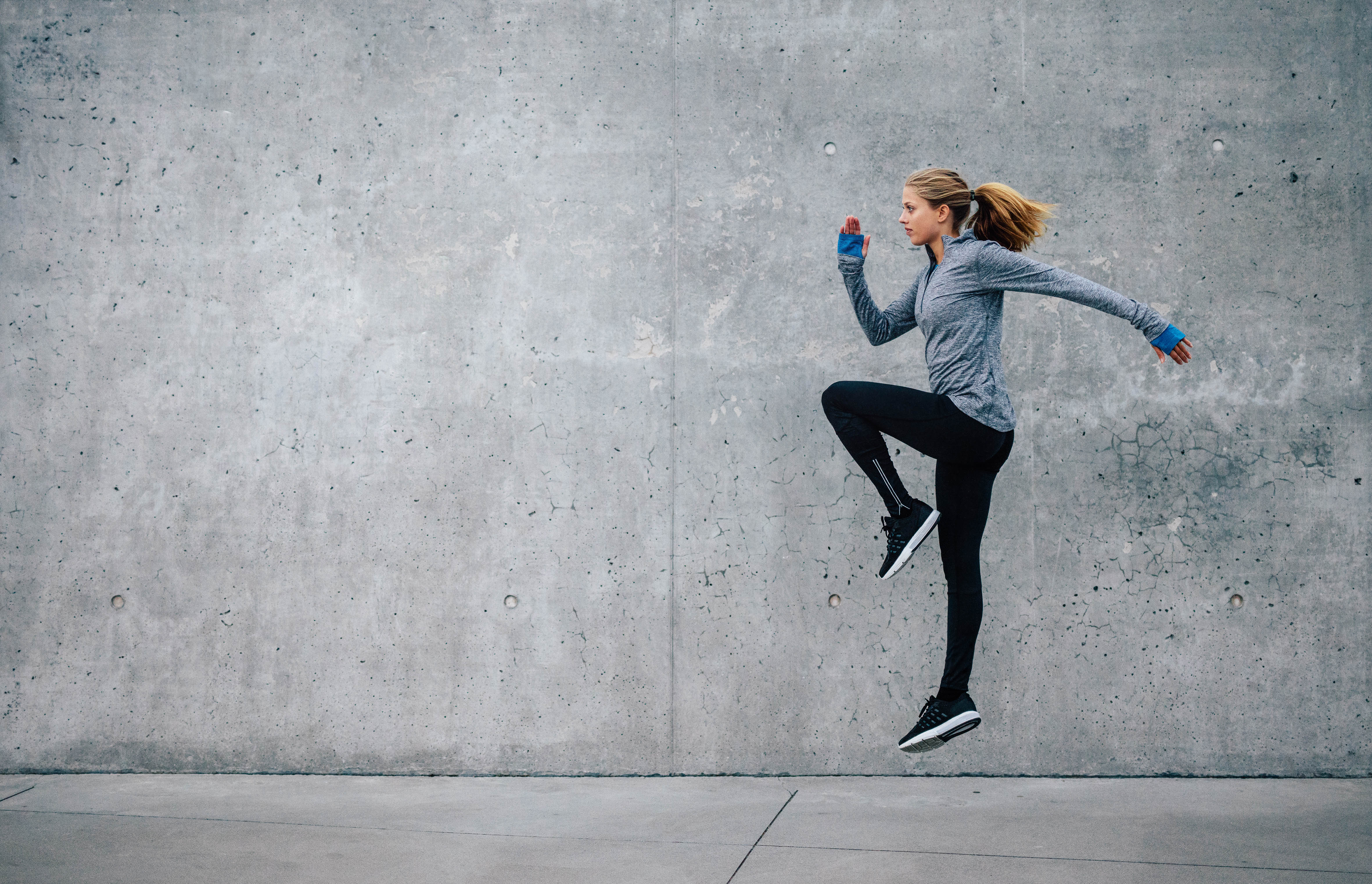 Young, fit woman doing vertical one legged jumps in front of a concrete wall Young, fit woman doing vertical one legged jumps in front of a concrete wall